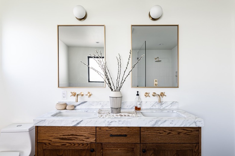 A vanity with marble countertops and two brass mirrors