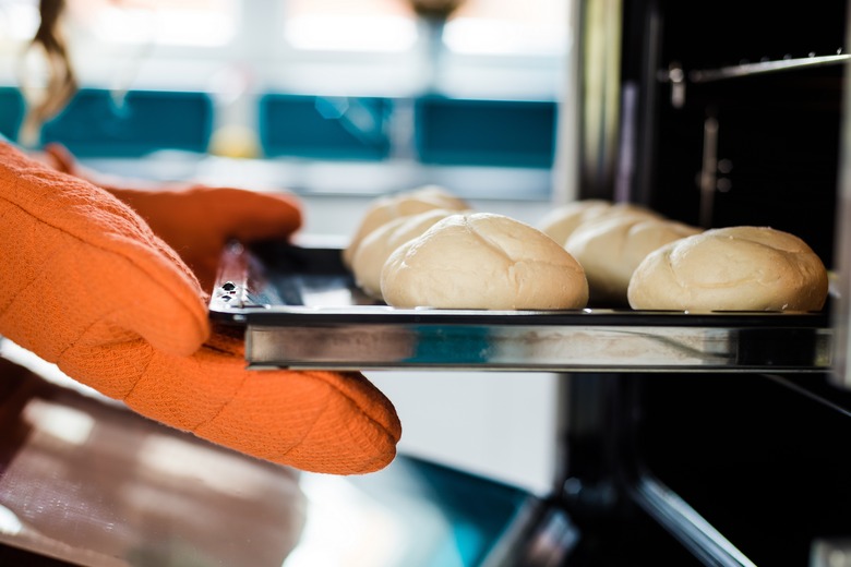 Baker hands with potholder next to metal cookie sheet