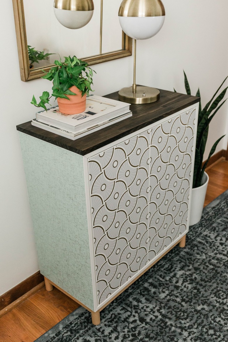 DIY entryway cabinet with plant, lamp, and books on hardwood floor with blue rug and plant against white wall with mirror