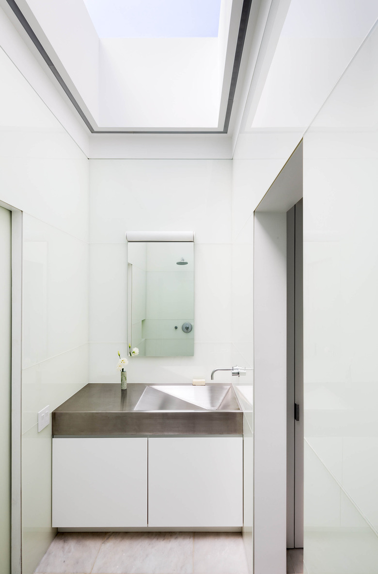 stainless steel bathroom sink in white space with white vanity cabinet and skylight