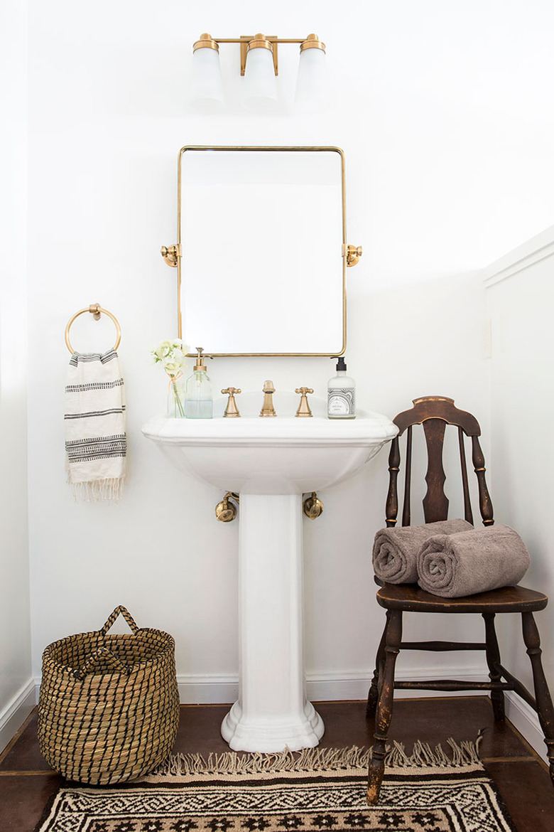 White bathroom pedestal sink with brass accents and area rug on wood floor