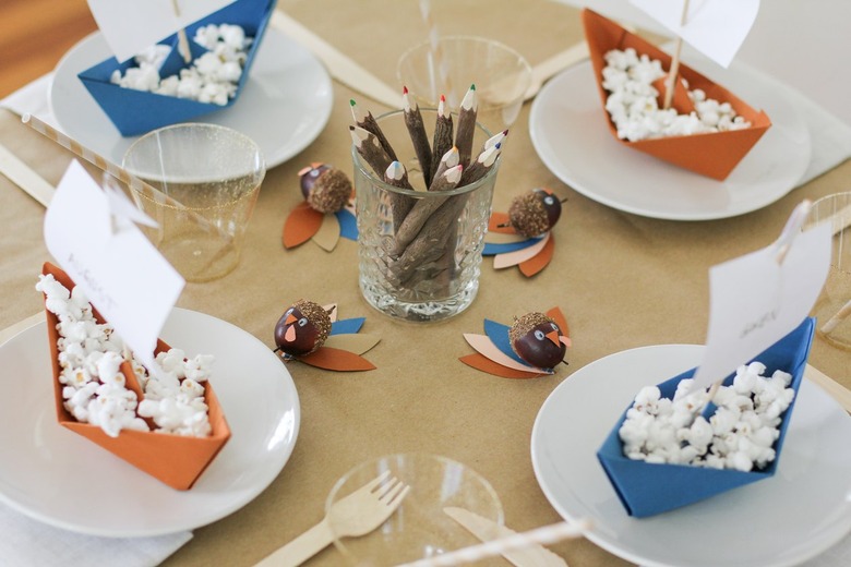 Kids table with folded paper boats, thanksgiving decorations, disposable dishware