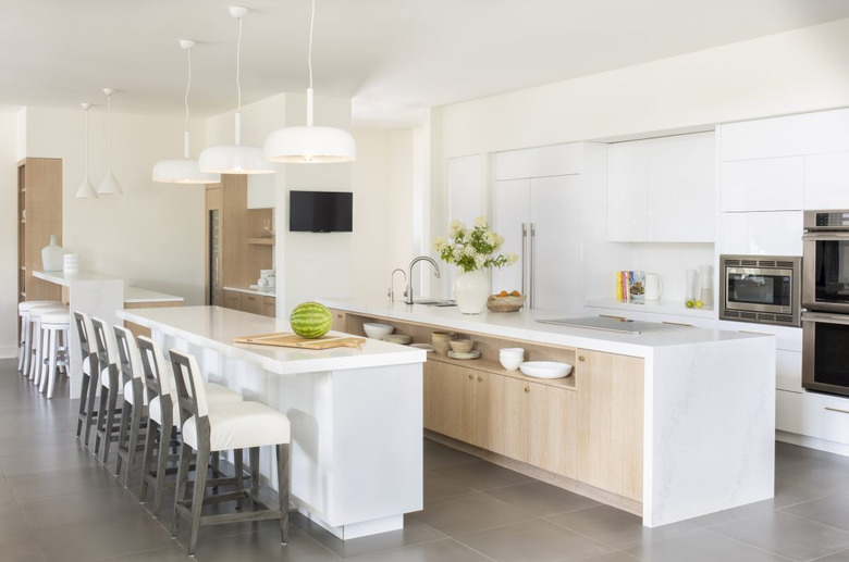 Long kitchen island storage with wood cabinets and marble waterfall countertop