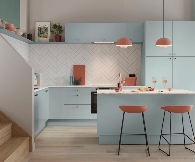 A light blue kitchen with orange pendant lights, orange bar stools, and white diagonal subway tile.