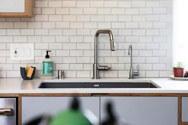 A white subway tile backsplash with a kitchen sink that has a one-handled silver faucet