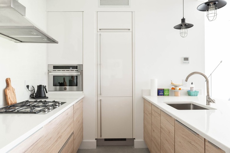 White contemporary kitchen with white countertops, wood cabinets, black stove burners, and silver sink and faucet