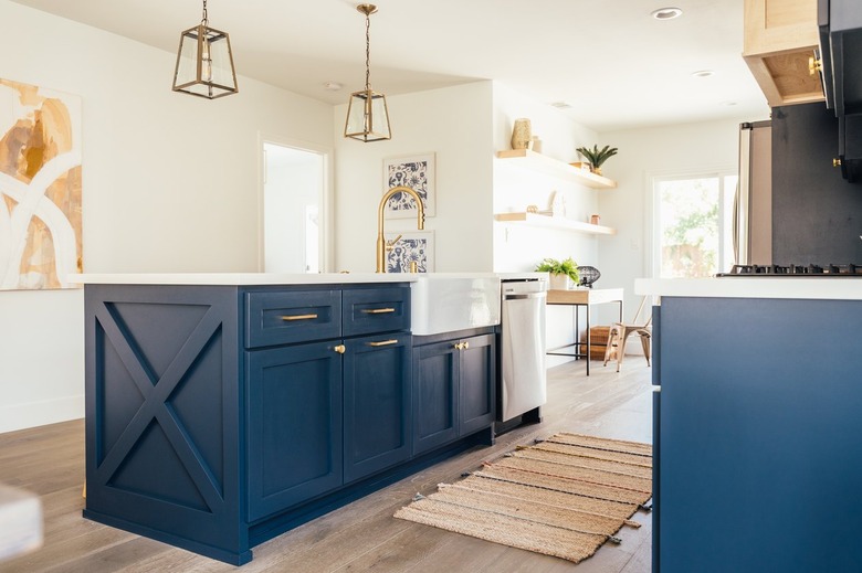 Dark blue kitchen island with gold lantern pendant lights. Light wood floor with beige striped rug.