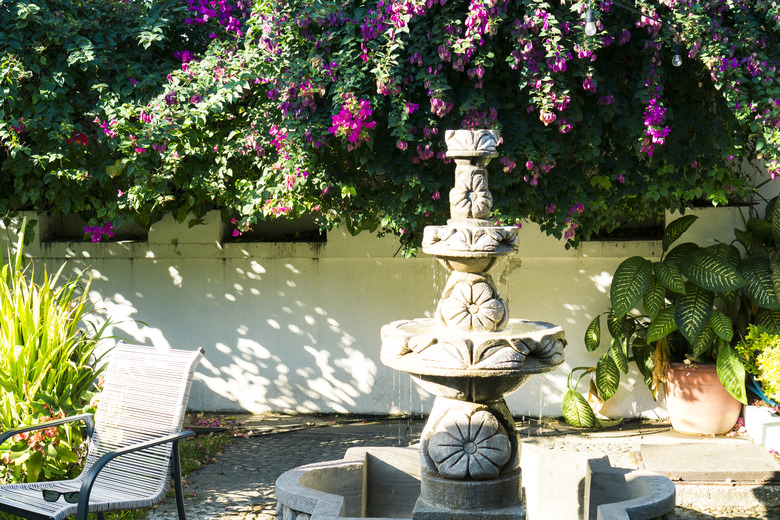 Garden with blooming flowers, plants and trees. Chairs and table in the park with fountain