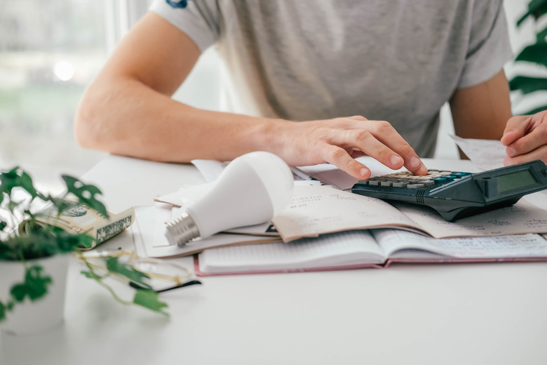 A man counts a bill on a calculator and a check for electricity on the table. Payment of utility services. Saving energy and money concept.