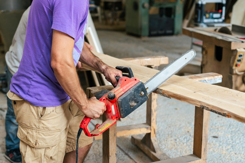 Manual wood concept. Profile side view cropped photo of cabinetmaker handyman tradesman holding chainsaw in hands sawing wood board make furniture in work shop or workroom