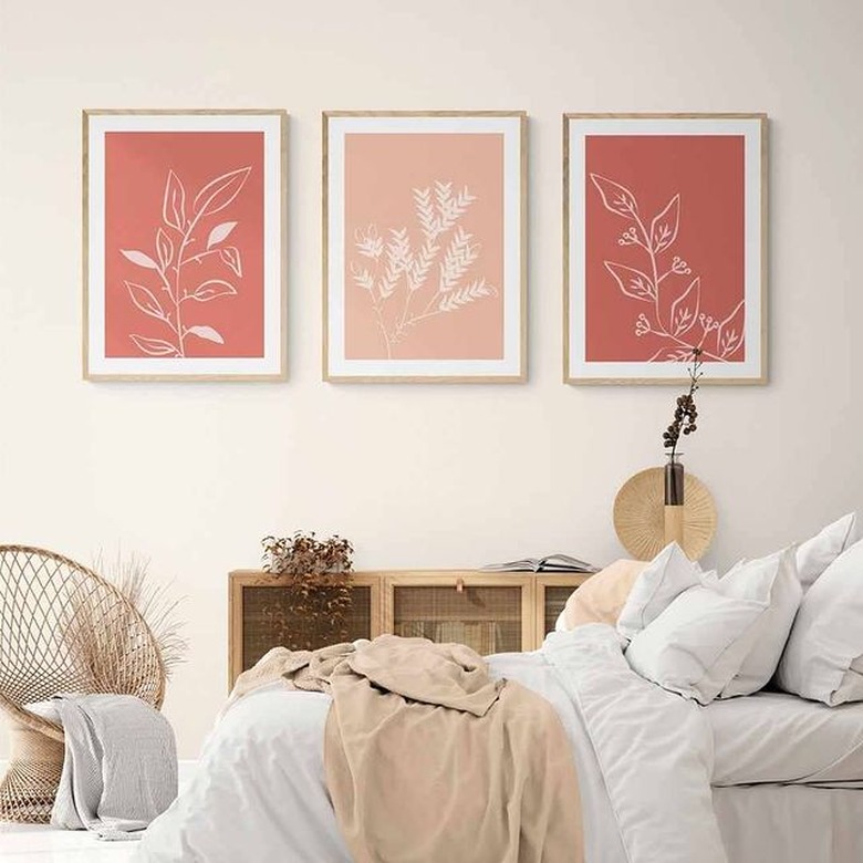 three pink plant art prints on wall above bed with white linens