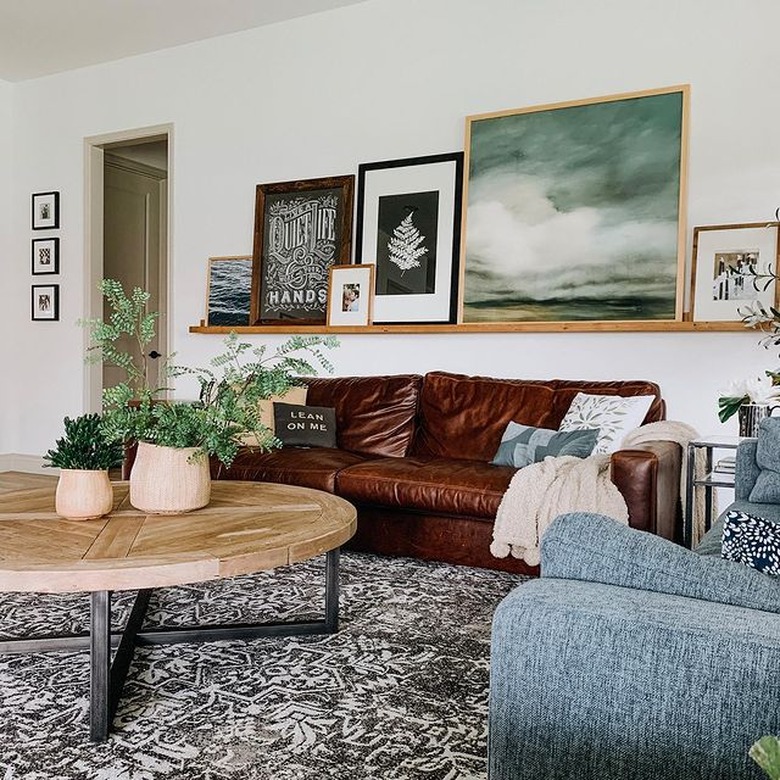 living room with wood shelf of framed art pieces and brown leather couch