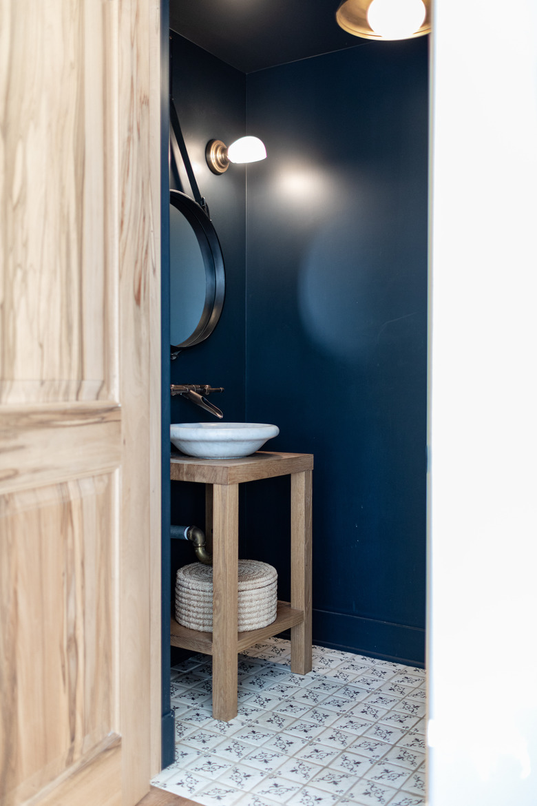 bathroom with navy walls, bowl sink, circular mirror and decorative floor tiles