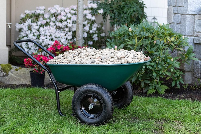 A green wheelbarrow full of white rocks on top of a green lawn