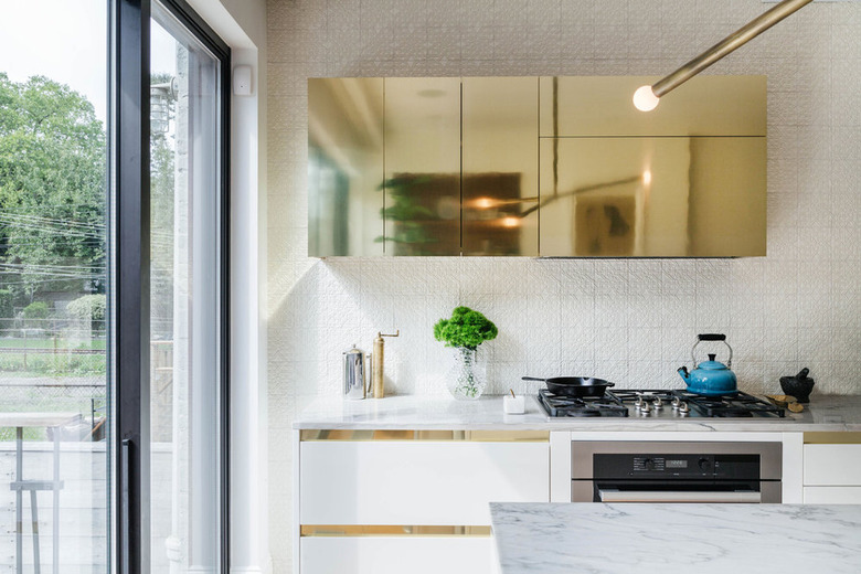 White kitchen with brass upper cabinets and white lower cabinets with brass reveal