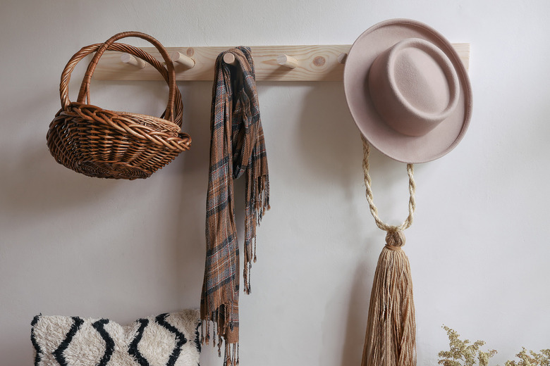 DIY wooden peg rail on wall with baskets, scarf and hat hanging from it