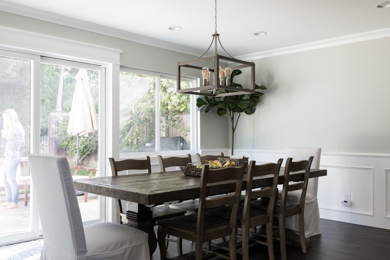 Dining room with dark wood furniture and a box chandelier. A tree plant. The walls are gray, with white wainscoting and millwork.