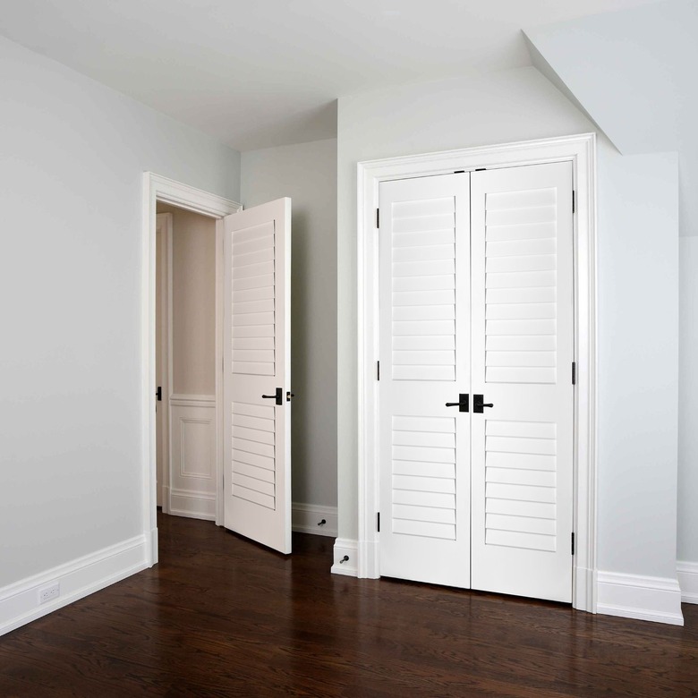 A white louvered closet door in a bedroom