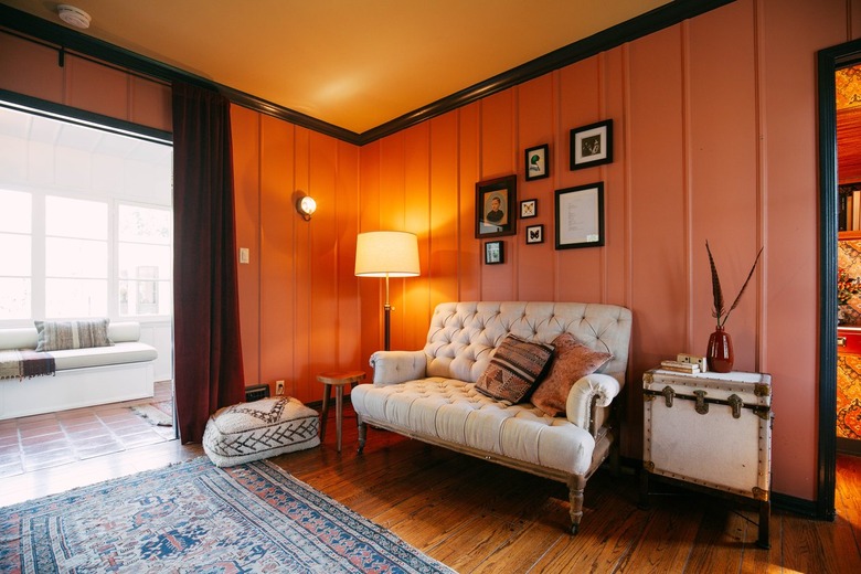 Ranch living room with pink walls, dark wood floor, victorian sofa, white vintage trunk side table with vase of feathers