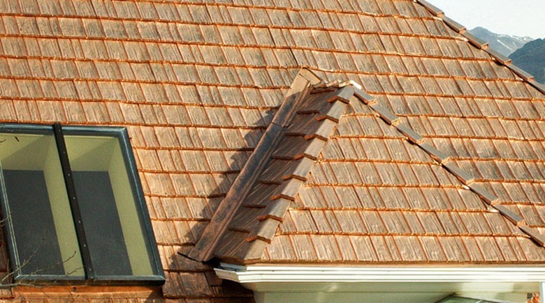 A copper metal roof with a black attic window