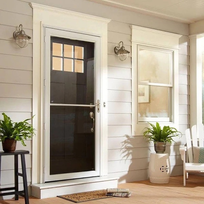 A storm door that covers a black craftsman-style door on a house with white siding and a large front porch