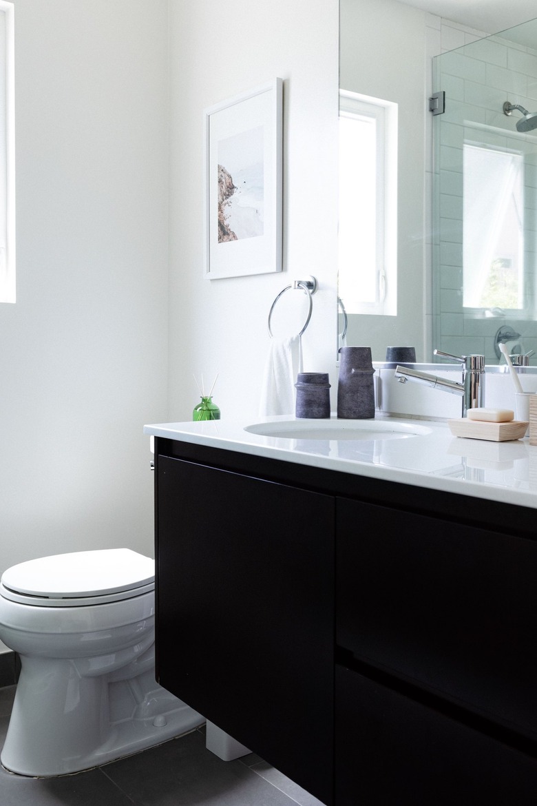 white toilet and dark wood vanity with white bathroom countertop and chrome hardware