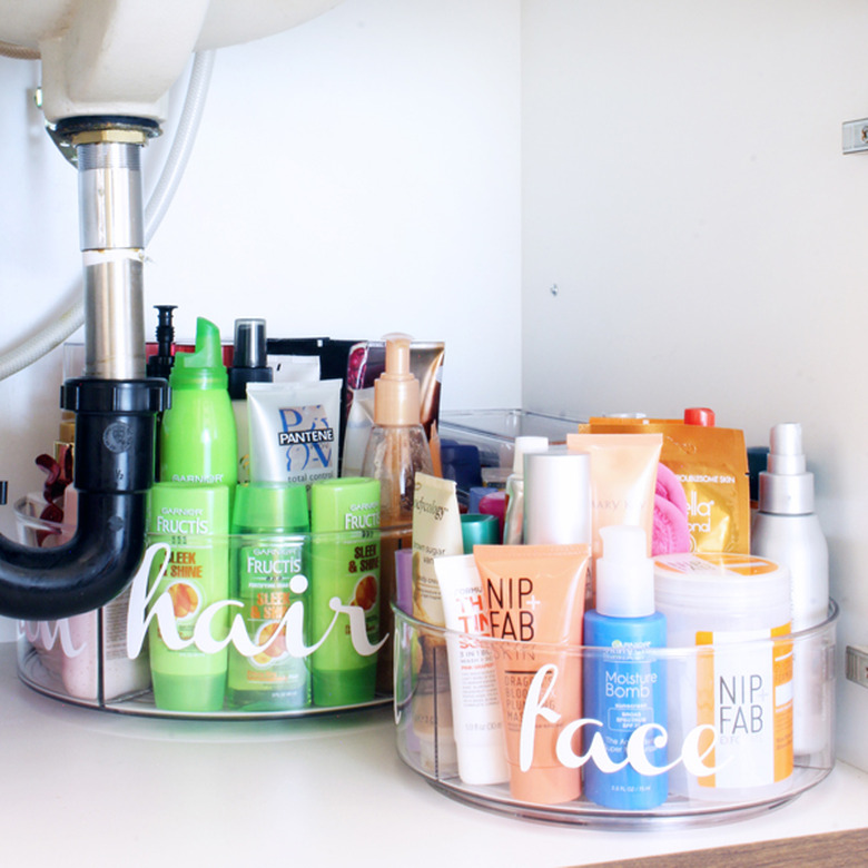 under sink storage with clear labeled containers with beauty products under bathroom sink