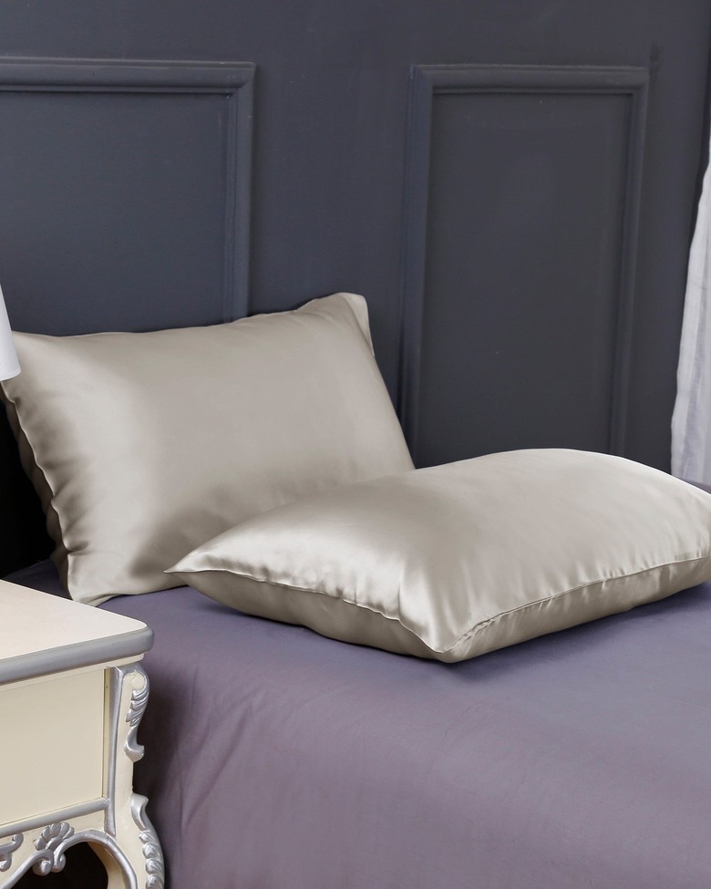 Two silk pillow cases on a purple bed with a navy headboard.