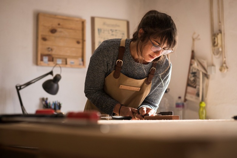 A woman wearing glasses and an apron works in a wood shop .