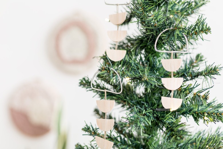 Scandi wood tree ornaments hanging off of small pine tree against white background