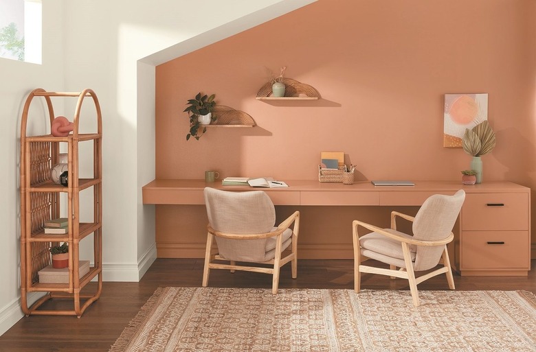 Desert-colored desk with two chairs in front of an accented desert-colored wall next to a white wall with a shelf