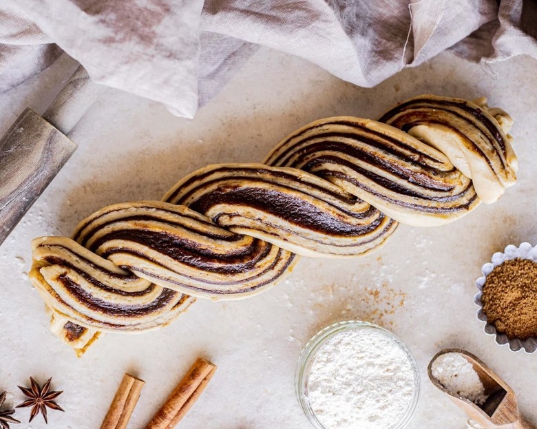 Vegan chocolate babka on a countertop with flour and a rolling pin off to the side.