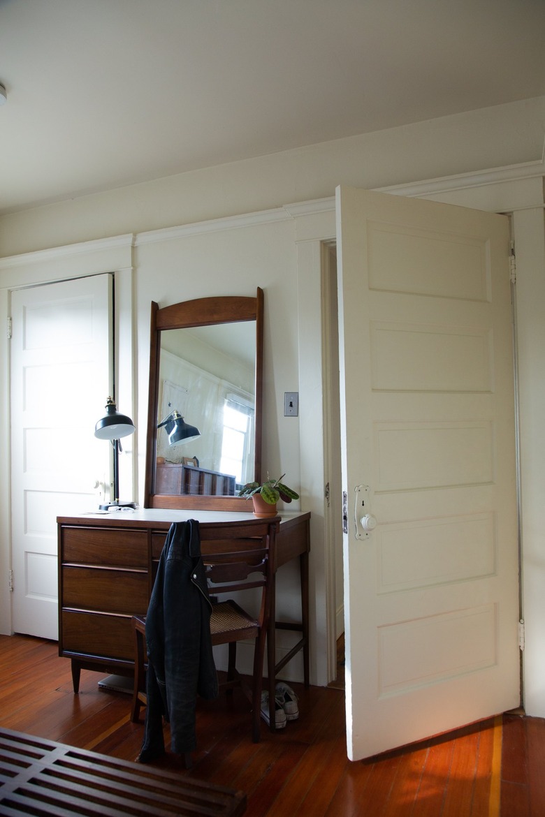 a swing-arm lamp and a mirror with a dark wooden frame on a dark-wood desk used as a dresser