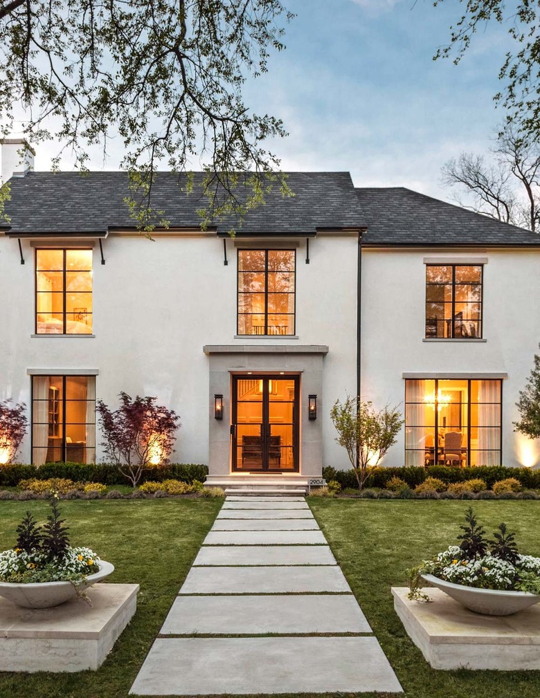 The outside of a white, two story home with light shining through windows.