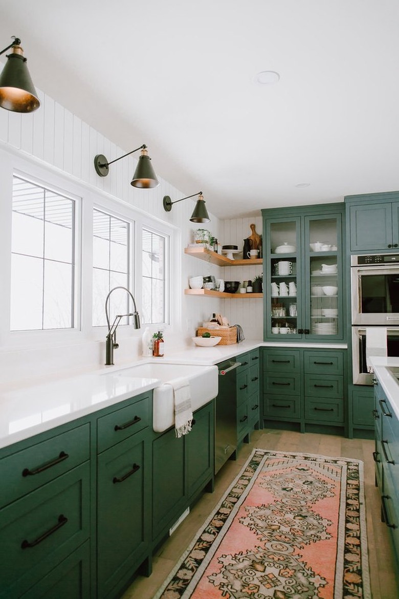 A white walled kitchen with green cabinets and a red antique runner rug.