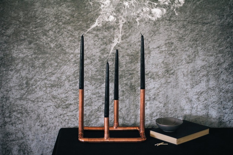 a candelabra made from copper pipe and four black taper candles