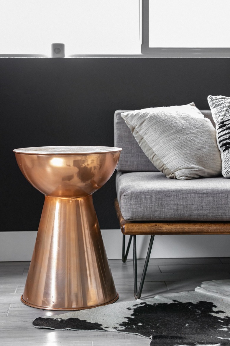 A drum side table with a gray sofa on a gray wood floor with an animal print rug