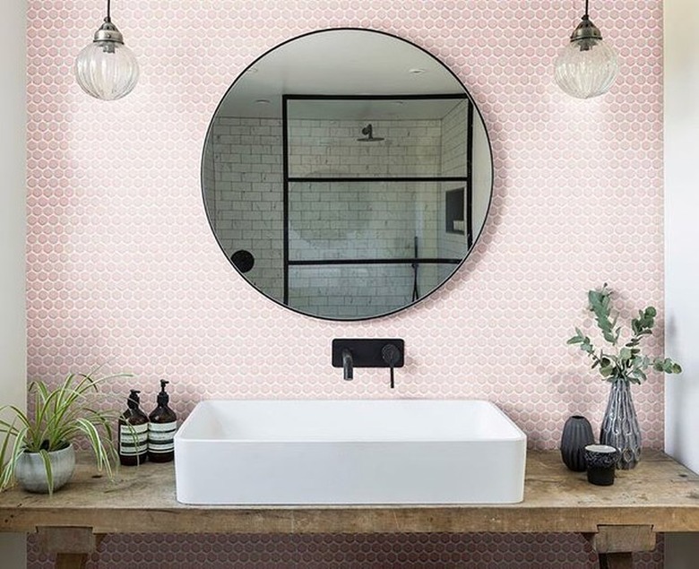 Modern rustic bathroom with white trough sink, pink hectaganol backsplash, black Wall-Mounted Bathroom Faucet, globe lamps, wood vanity.