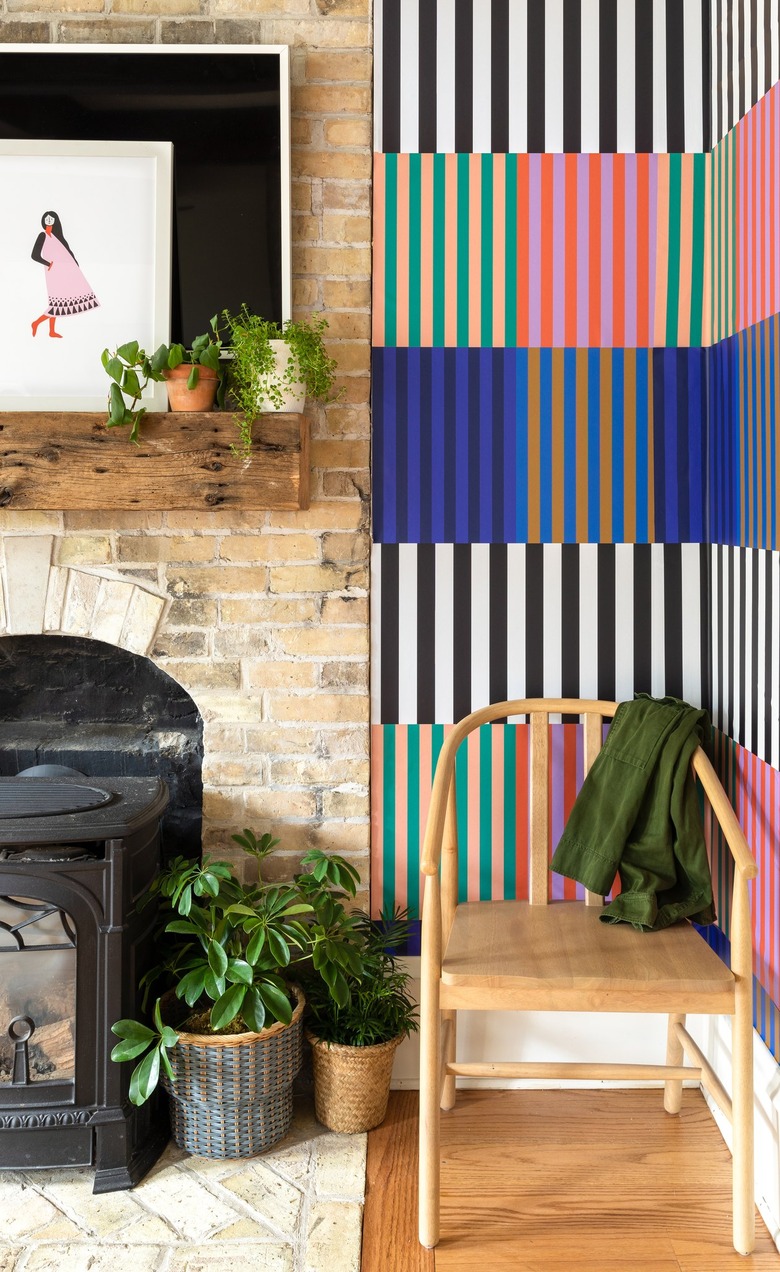 corner with fireplace and chair, with wall on the right side covered in striped wallpaper