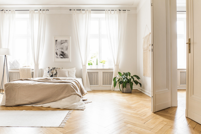 Bright bedroom with sheer white curtains, beige decorations, hardwood floor