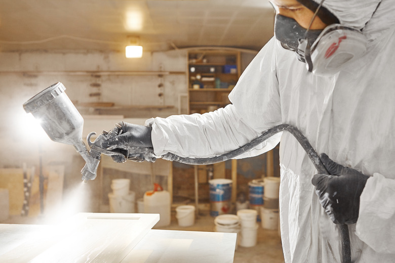 Wearing a respirator while painting wooden planks in workshop.