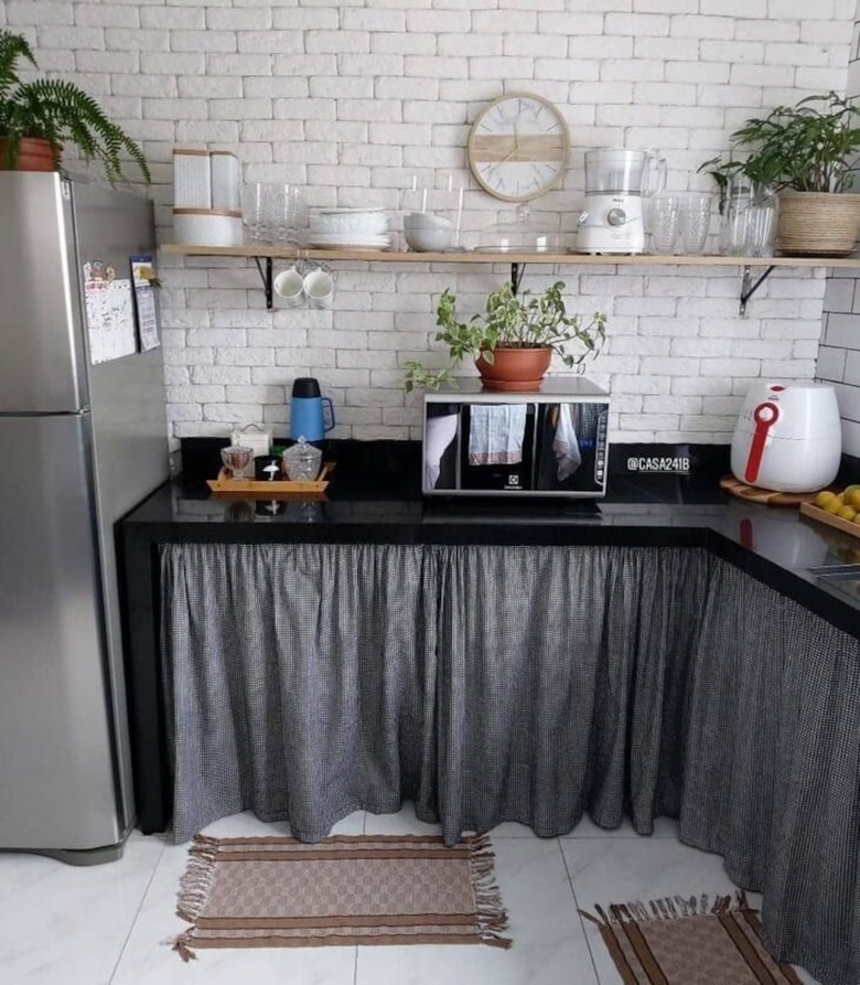 A gray pleated sink skirt installed over exposed pipes in a kitchen