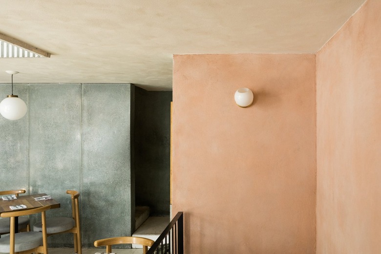 A restaurant dining area with gray and pink walls, globe sconces and pendant lights, curved wood dining chairs and wood tables.