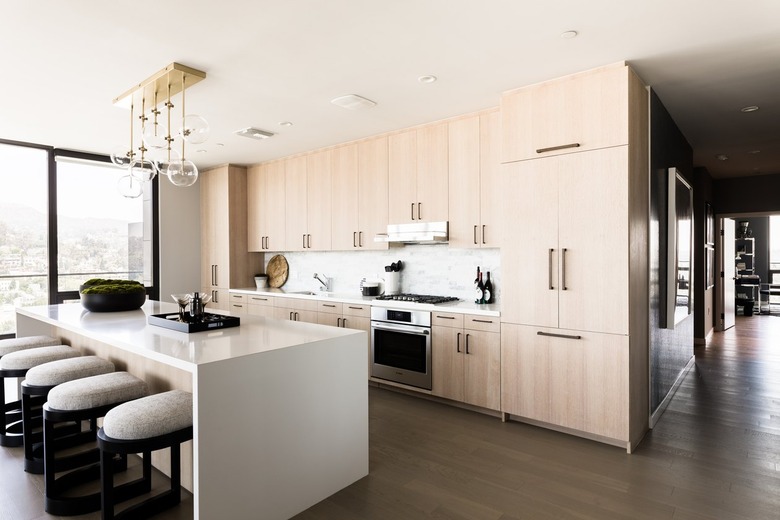 Countertops with Oak Cabinets in Bar stools at a white kitchen island, with a bar tray and bowls of moss decor. Globe pendant lights and light wood cabinets.