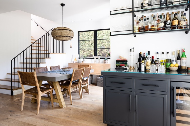 A white-walled, wood floored dining room with a gray cabinet bar and staircase