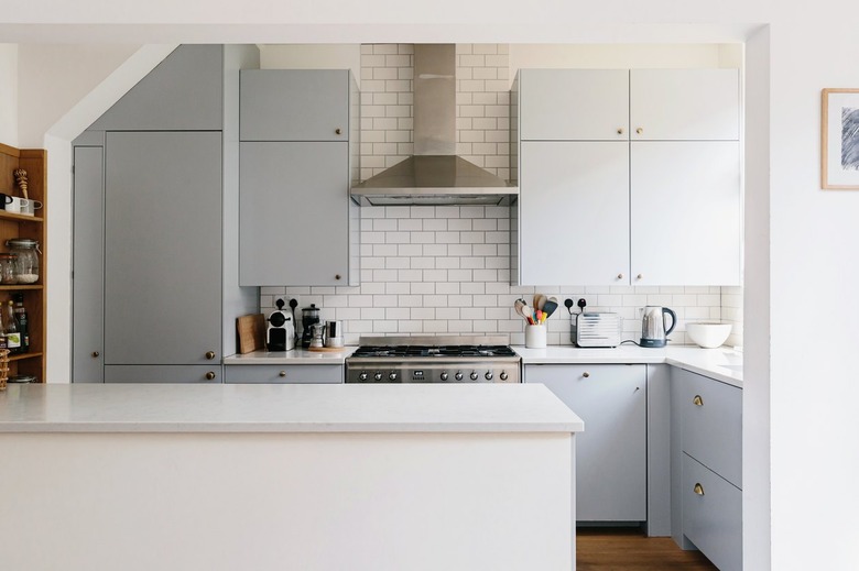 White kitchen with white-tiled backsplash. grey cabinets, white stone countertops, and silver stove