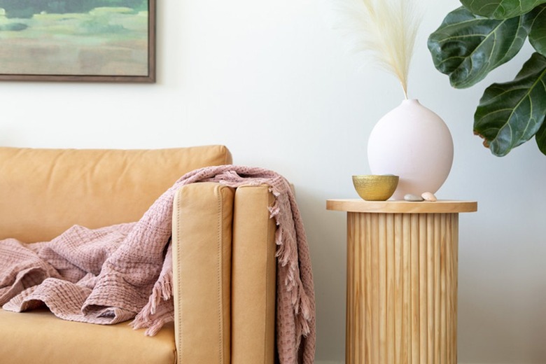 Fluted side table with dowel base, birch circle board tabletop, round pink vase and gold bowl, neutral sofa, and pink blanket