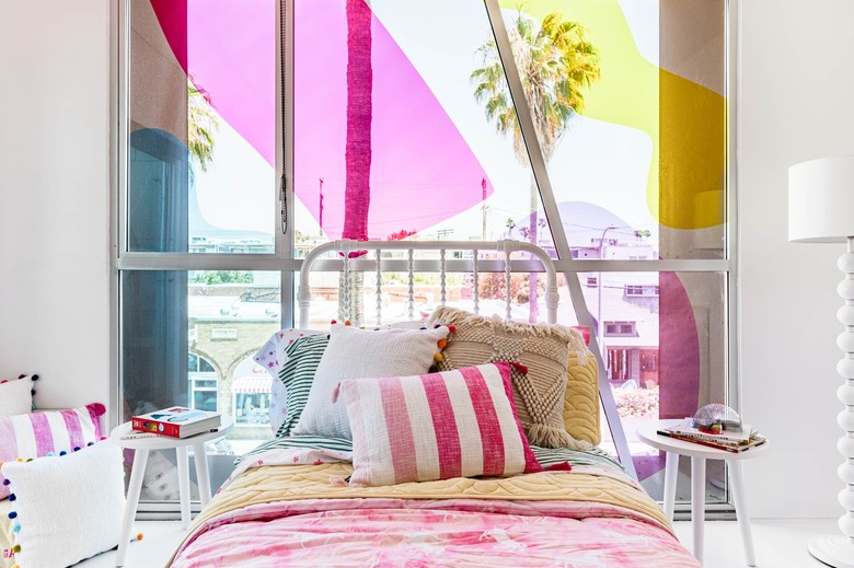 Pink and yellow themed kid's room with colorful bedding, throw pillows, and white furniture