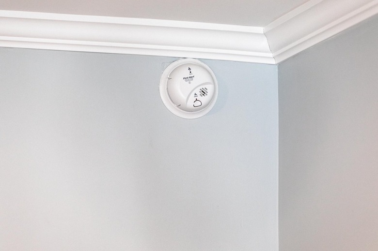 A wired smoke detector installed on a light gray wall near the ceiling.