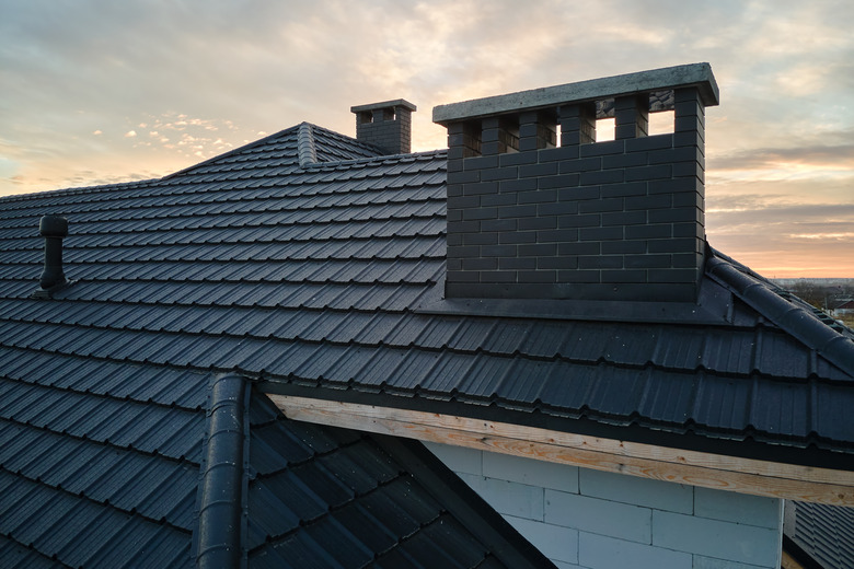 Closeup of brick chimney on house roof top covered with ceramic shingles. Tiled covering of building